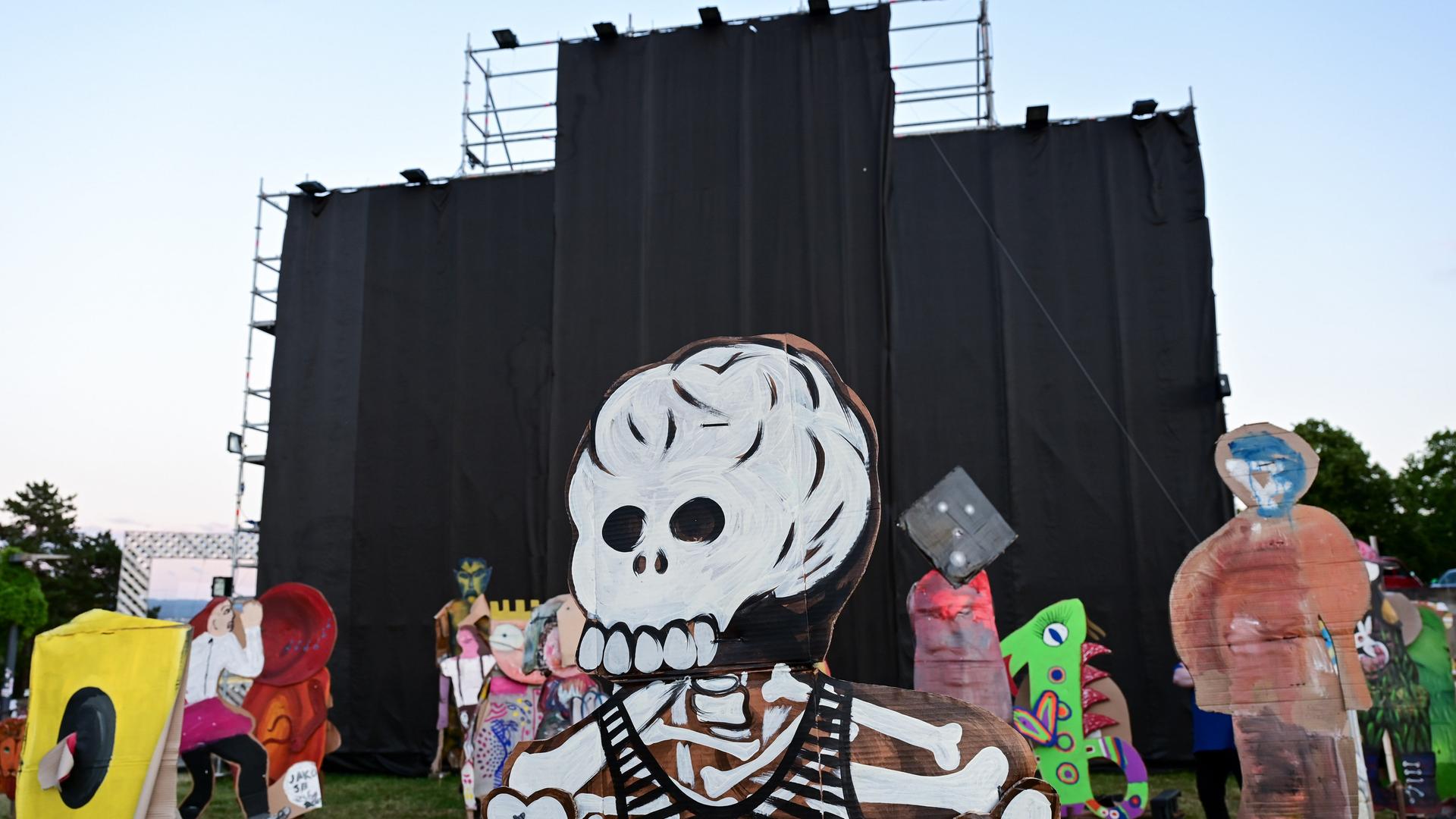 Von einem Metallgerüst hängen schwarze Stoffbahnen herunter. Auf der Wiese davor stehen Pappfiguren, die vorderste davon in Gestalt eines Skeletts mit Totenschädel. Von einem Metallgerüst hängen schwarze Stoffbahnen herunter. Auf der Wiese davor stehen Pappfiguren, die vorderste davon in Gestalt eines Skeletts mit Totenschädel.