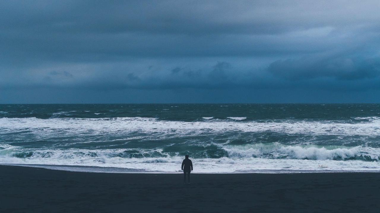 Zu sehen: Ein Mann steht am Ufer eines Meeres. Zu sehen: Ein Mann steht am Ufer eines Meeres.