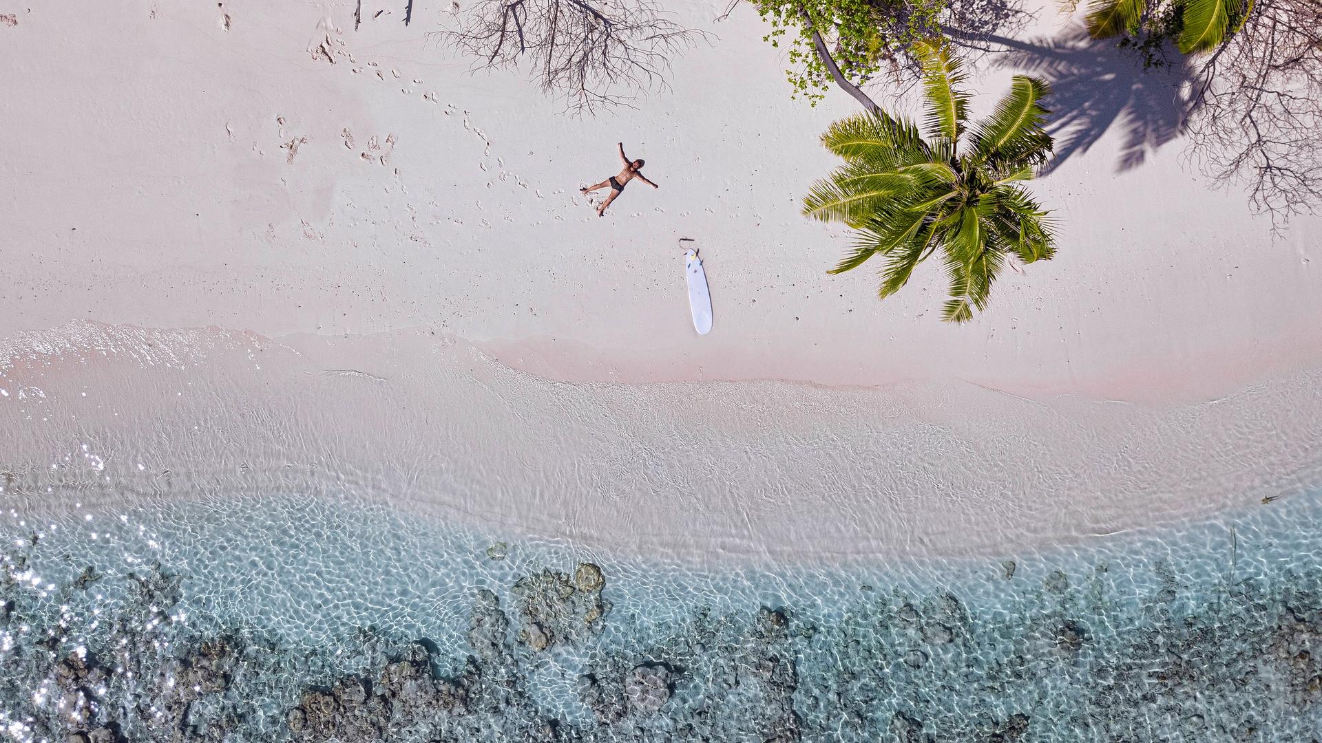 Ein Mann liegt mit einem Surfboard an einem einsamen Strand. Ein Mann liegt mit einem Surfboard an einem einsamen Strand.