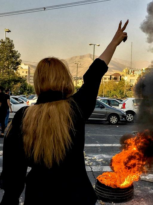 Feuer auf der Straße, eine Frau streckt den Arm in die Höhe.