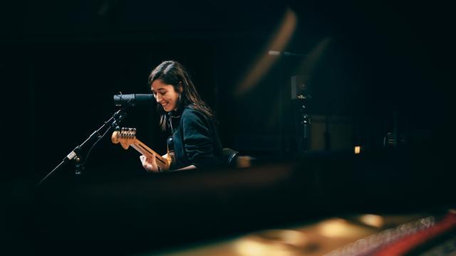 Eine junge Frau steht lachend vor einem Mikrofon mit ihrer Gitarre. Oska im Kammermusiksaal des Deutschlandfunks in Köln.