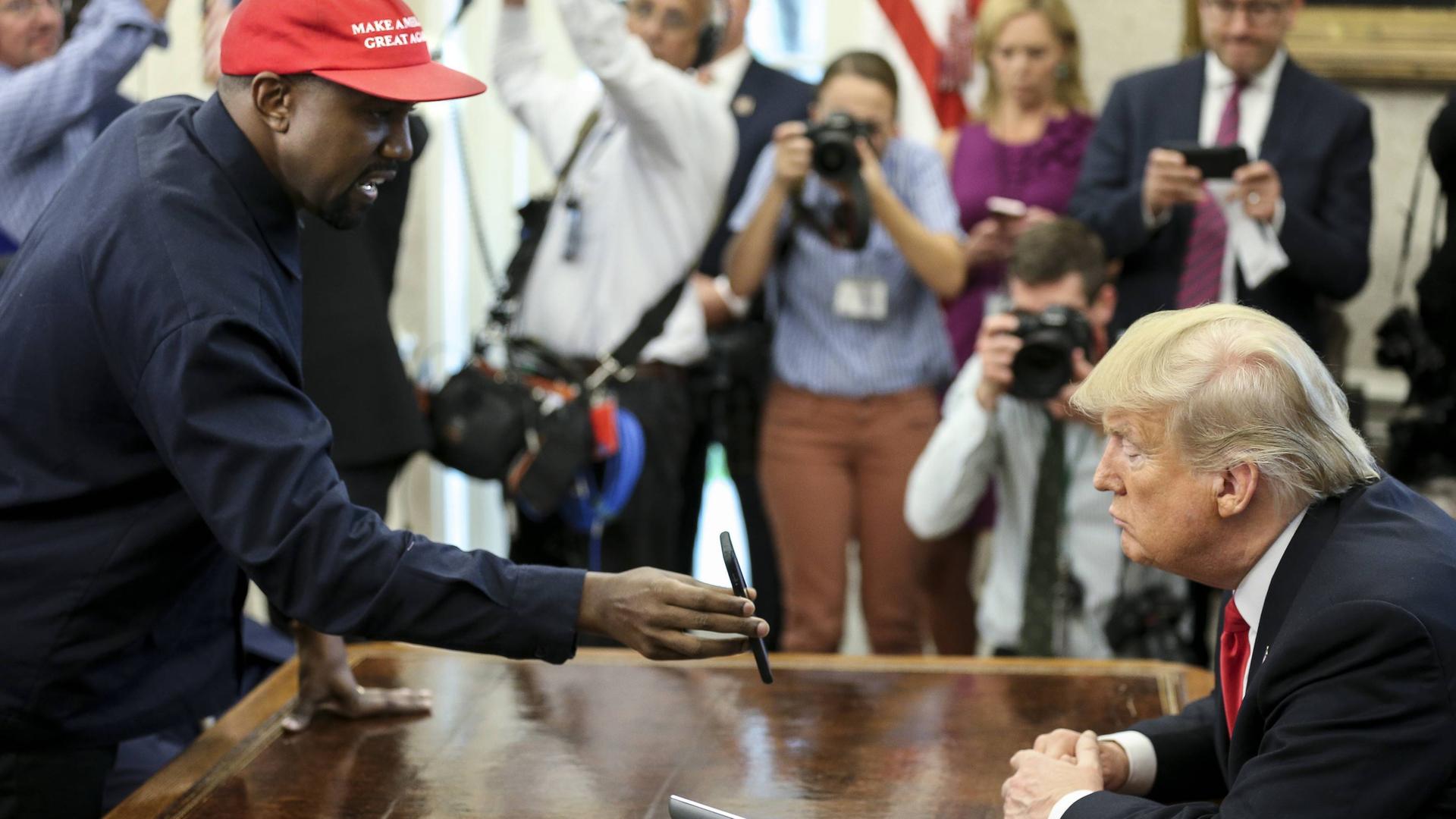 Kanye West zeigt Donald Trump sein Handy, umringt von Fotografen. Kanye West zeigt Donald Trump sein Handy, umringt von Fotografen.