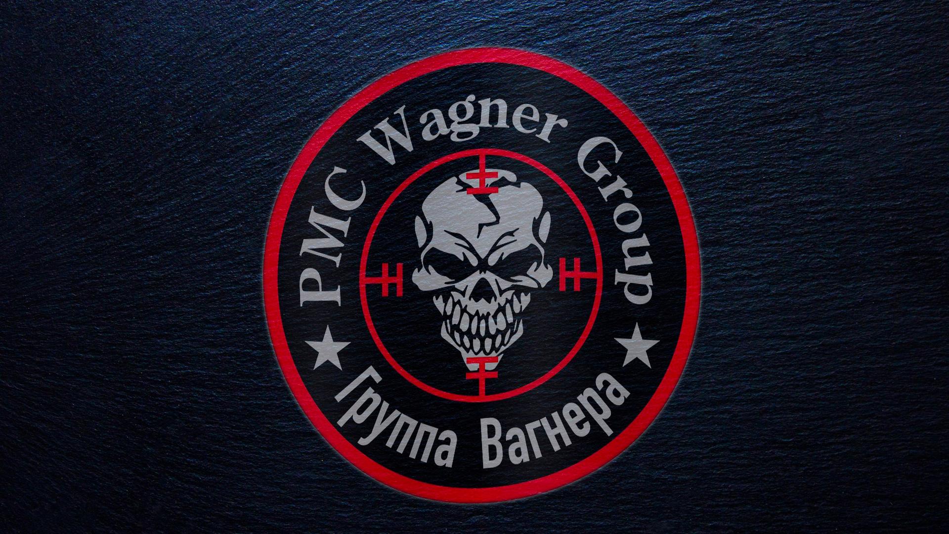 In einem inneren roten Kreis ist ein grinsender Totenkopf abgebildet, in einem äußeren die Schrift "PMC Wagner Group" sowie kyrillische Schrift. Der Hintergrund ist schwarz. In einem inneren roten Kreis ist ein grinsender Totenkopf abgebildet, in einem äußeren die Schrift "PMC Wagner Group" sowie kyrillische Schrift. Der Hintergrund ist schwarz.