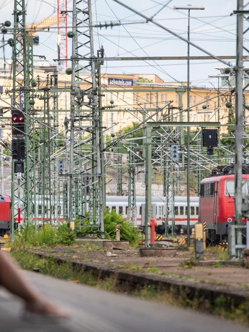 Eine Frau sitzt an einem Bahnsteig des Stuttgarter Hautpbahnhofs. Im Hintergrund sind Züge und Oberleitungen zu sehen. 
