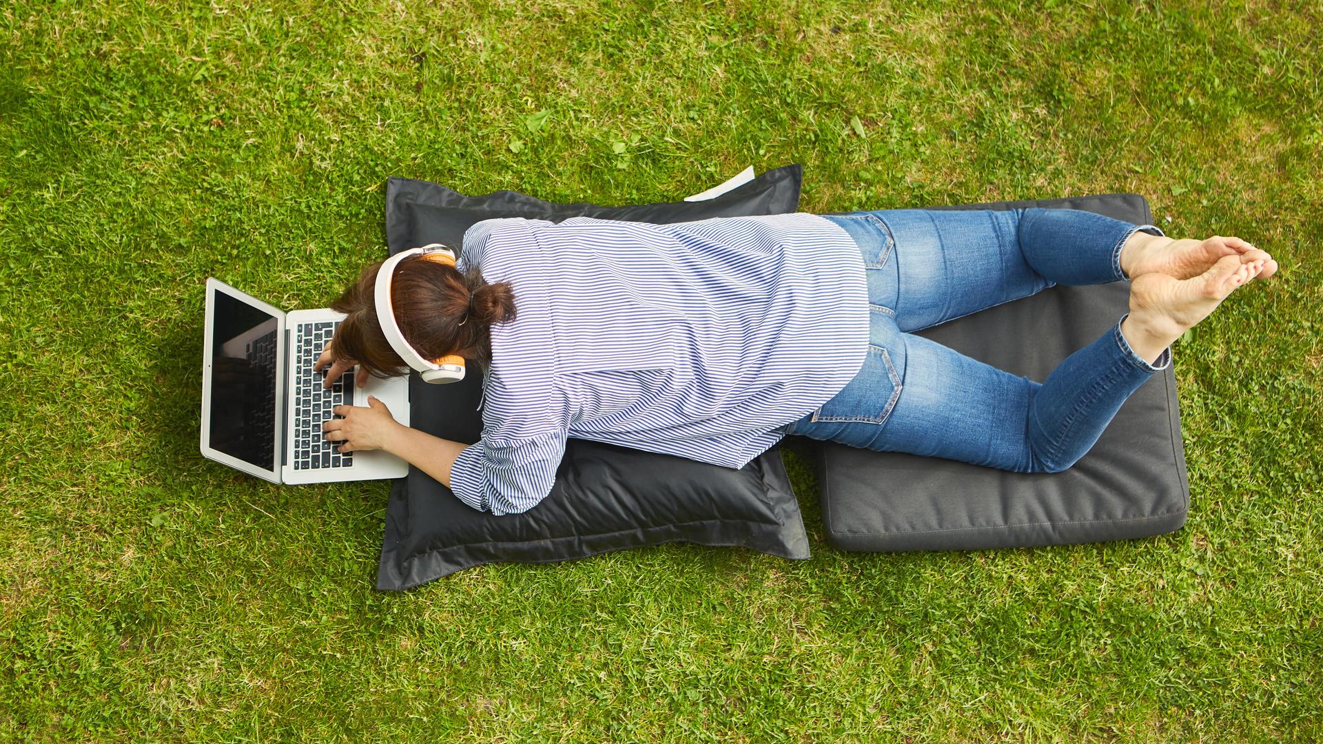 Frau am Laptop Computer bei Videokonferenz liegend auf einer Wiese. (Symbolbild) Frau am Laptop Computer bei Videokonferenz liegend auf einer Wiese. (Symbolbild)