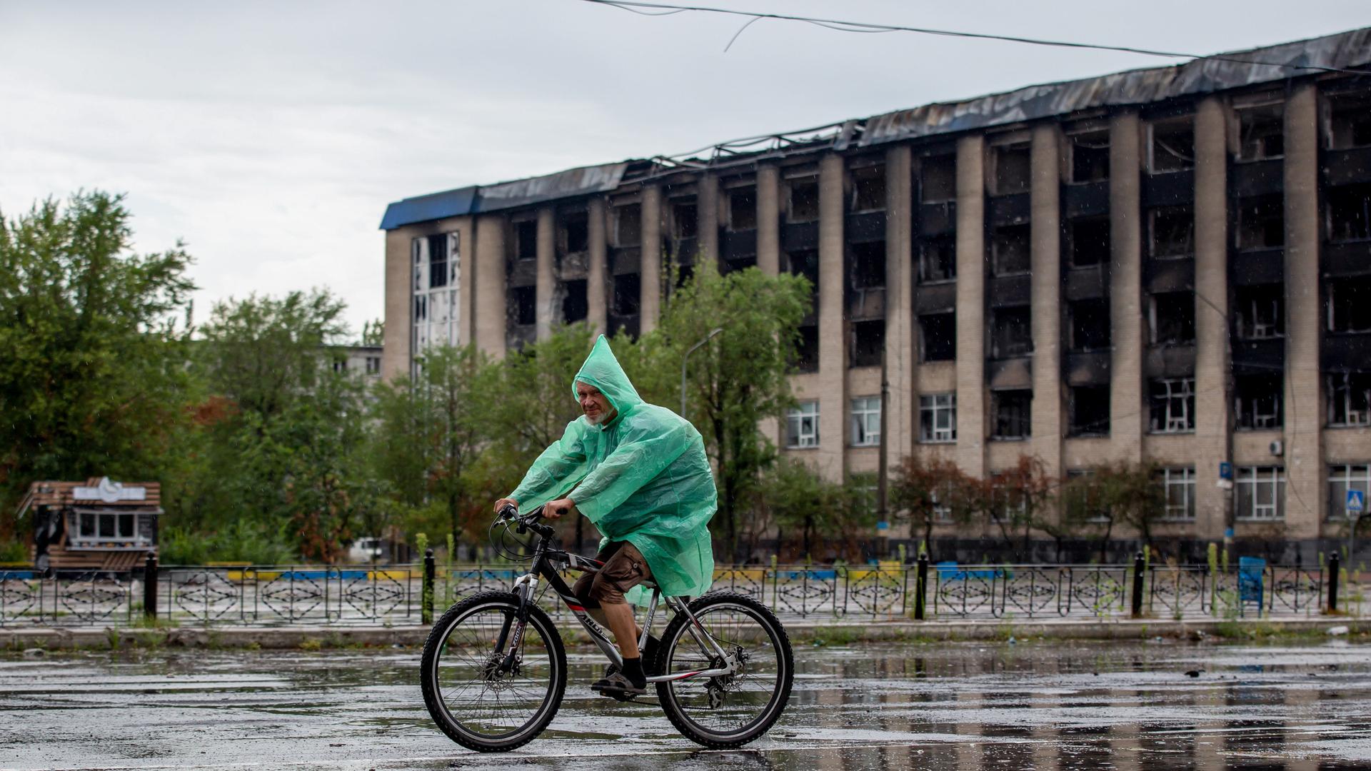 Aufnahme im russisch besetzten Severodonetsk: ein Radfahrer, dahinter eine ausgebranntes Gebäude.