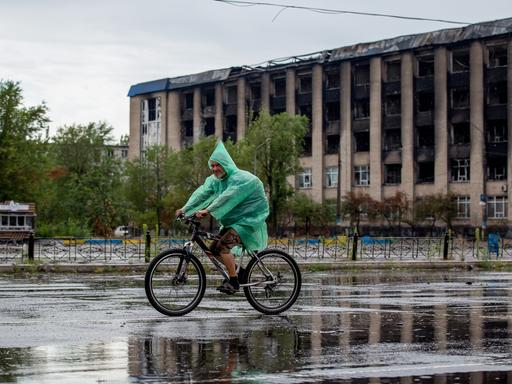 Aufnahme im russisch besetzten Severodonetsk: ein Radfahrer, dahinter eine ausgebranntes Gebäude.