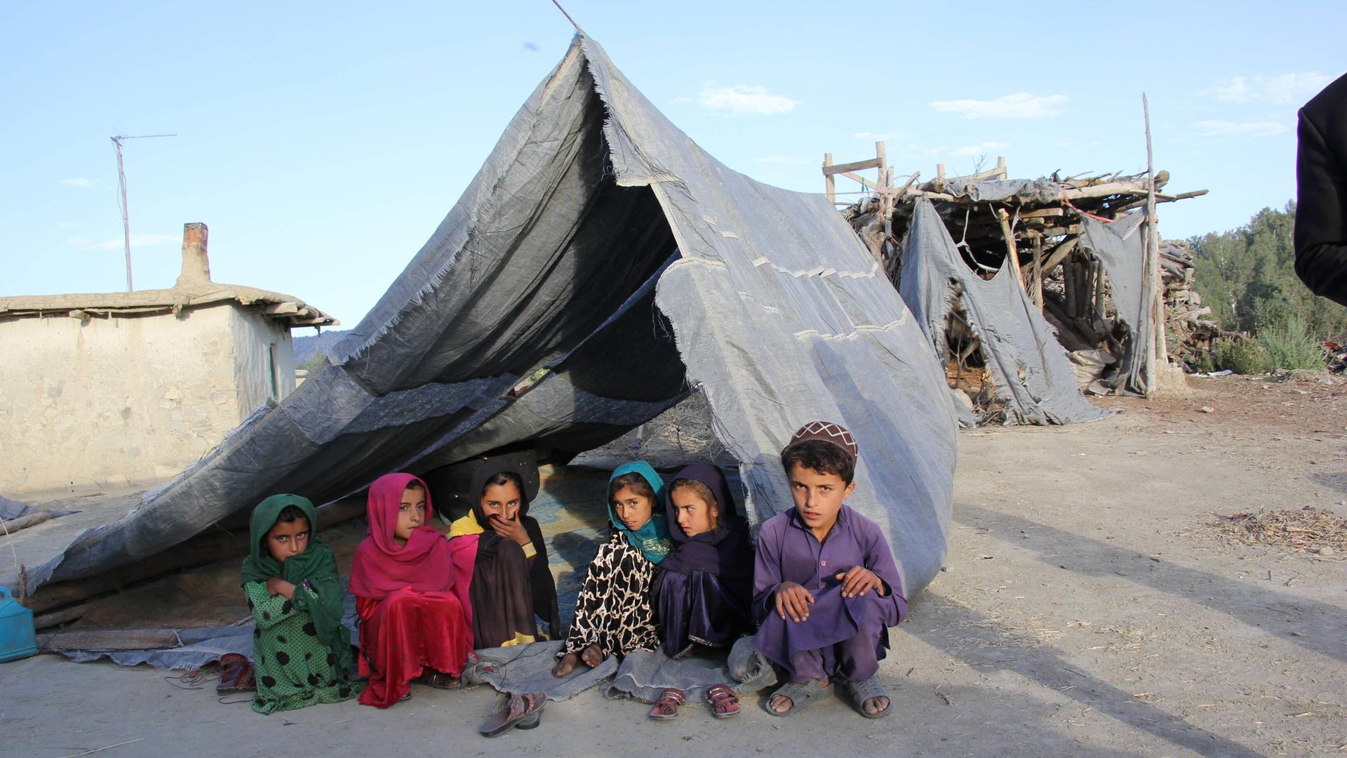 Afghanische Kinder sitzen unter einer Zeltplane auf dem Boden.