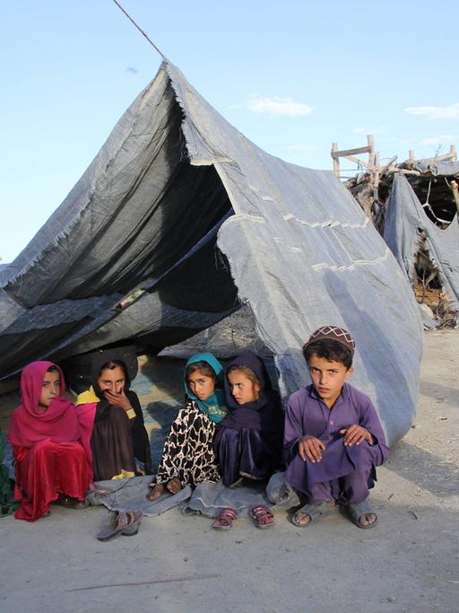 Afghanische Kinder sitzen unter einer Zeltplane auf dem Boden.