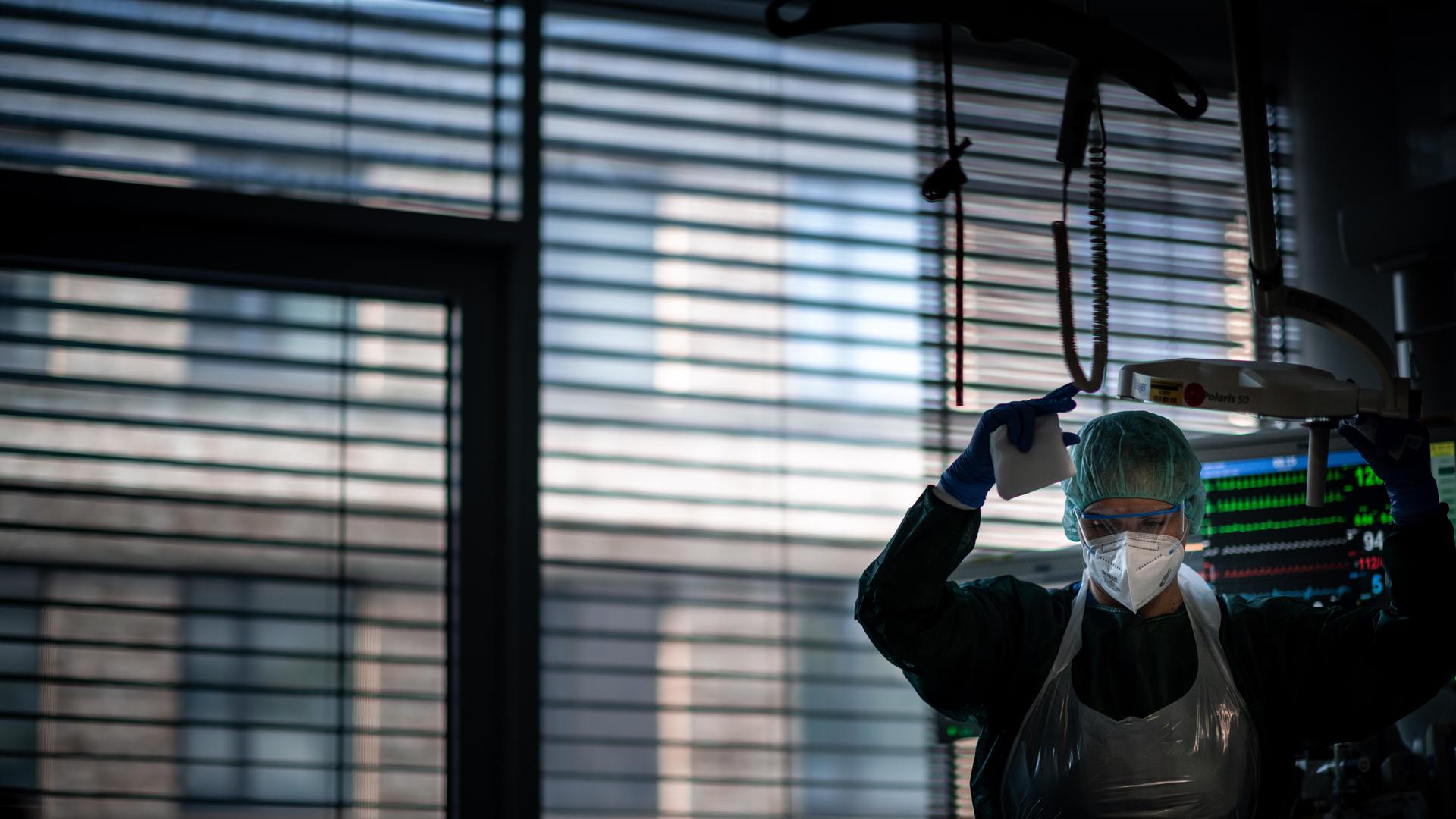 Eine Gesundheits- und Krankenpflegerin steht vor dem abgedunkelten Fenster in einem Corona-Intensivzimmer und behandelt einen Patienten.