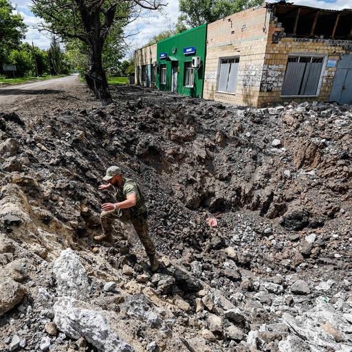 Ein ukrainischer Soldat steht in einem riesigen Krater neben einer Straße, das durch einen russischen Luftangriff entstanden sein soll.