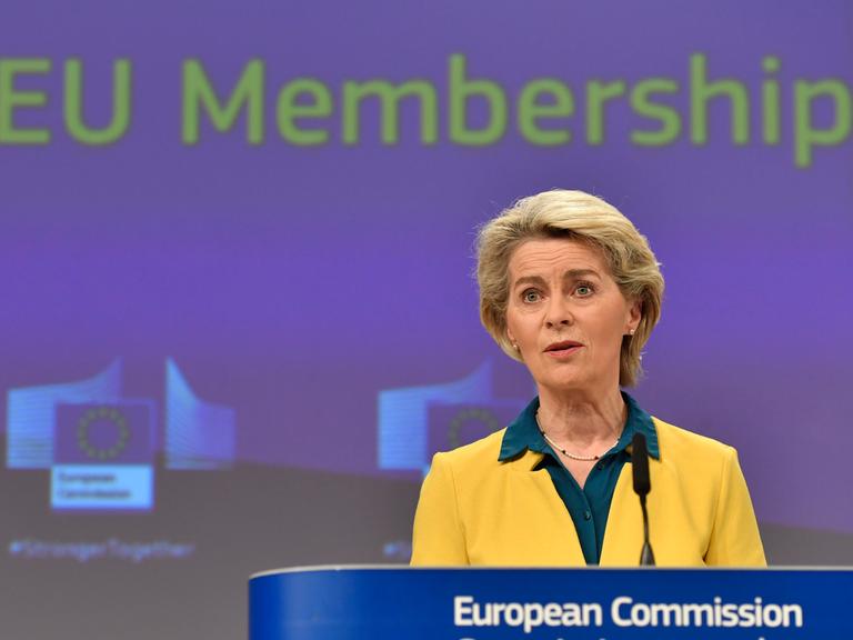 EU-Kommissionspräsidentin Ursula von der Leyen in gelbem Sakko vor einem blauen Hintergrund mit der Aufschrift EU Membership