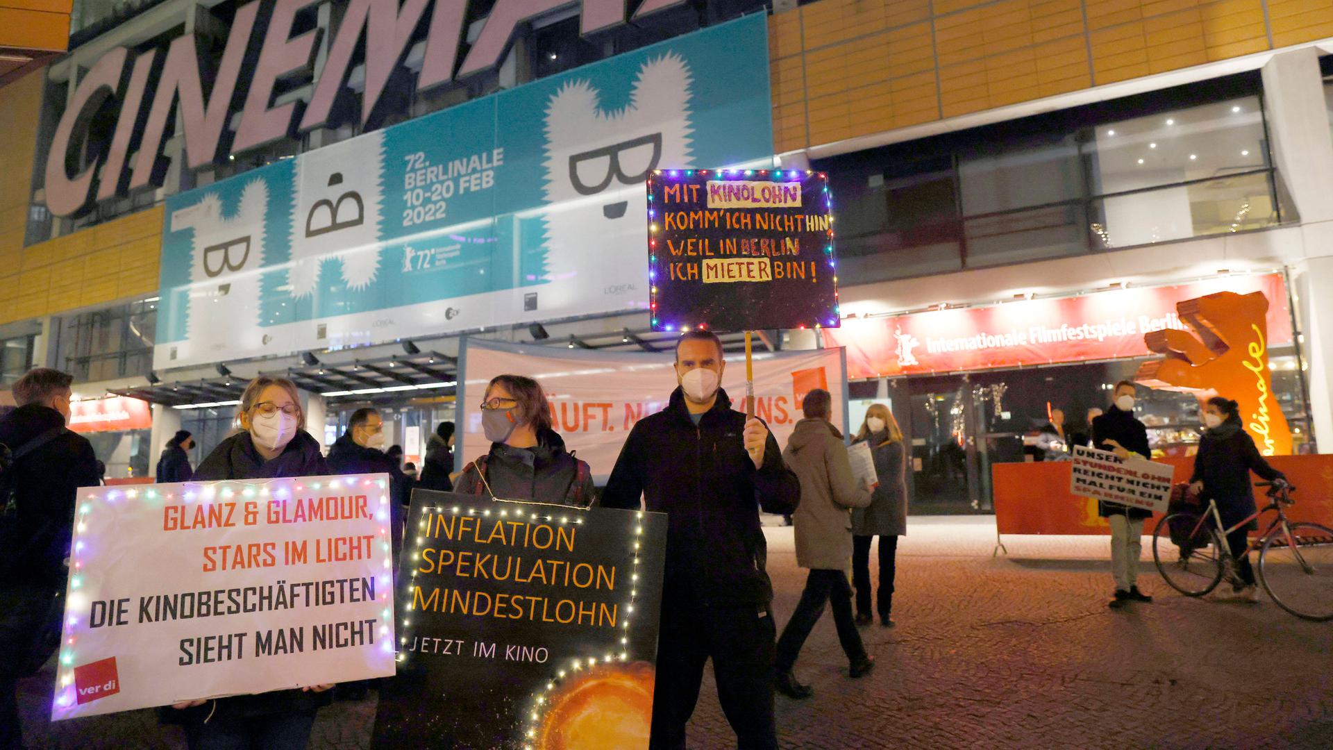 Mehrere Menschen stehen mit Plakaten vor einem Kino und demonstrieren. Auf einem steht beispielsweise: "Glanz und Glamour, Stars im Licht. Die Kinobeschäftigten sieht man nicht." Mehrere Menschen stehen mit Plakaten vor einem Kino und demonstrieren. Auf einem steht beispielsweise: "Glanz und Glamour, Stars im Licht. Die Kinobeschäftigten sieht man nicht."