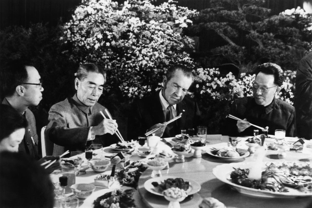 Männer in Anzügen sitzen um einen Tisch und essen mit Stäbchen.
