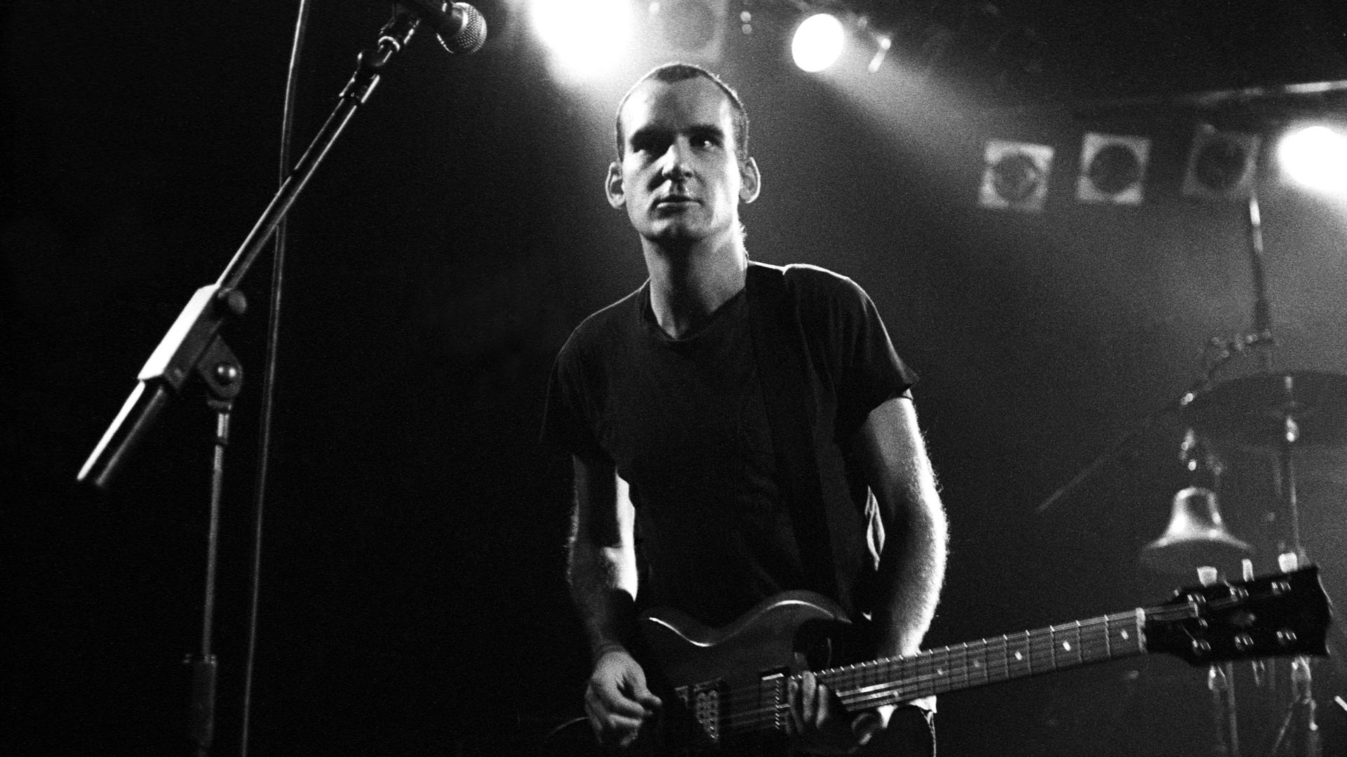 Ian MacKaye steht bei einem Konzert seiner Band Fugazi auf der Bühne und spielt Gitarre. Ian MacKaye steht bei einem Konzert seiner Band Fugazi auf der Bühne und spielt Gitarre.