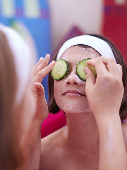 Zwei Mädchen legen sich Gesichtsmasken auf.
