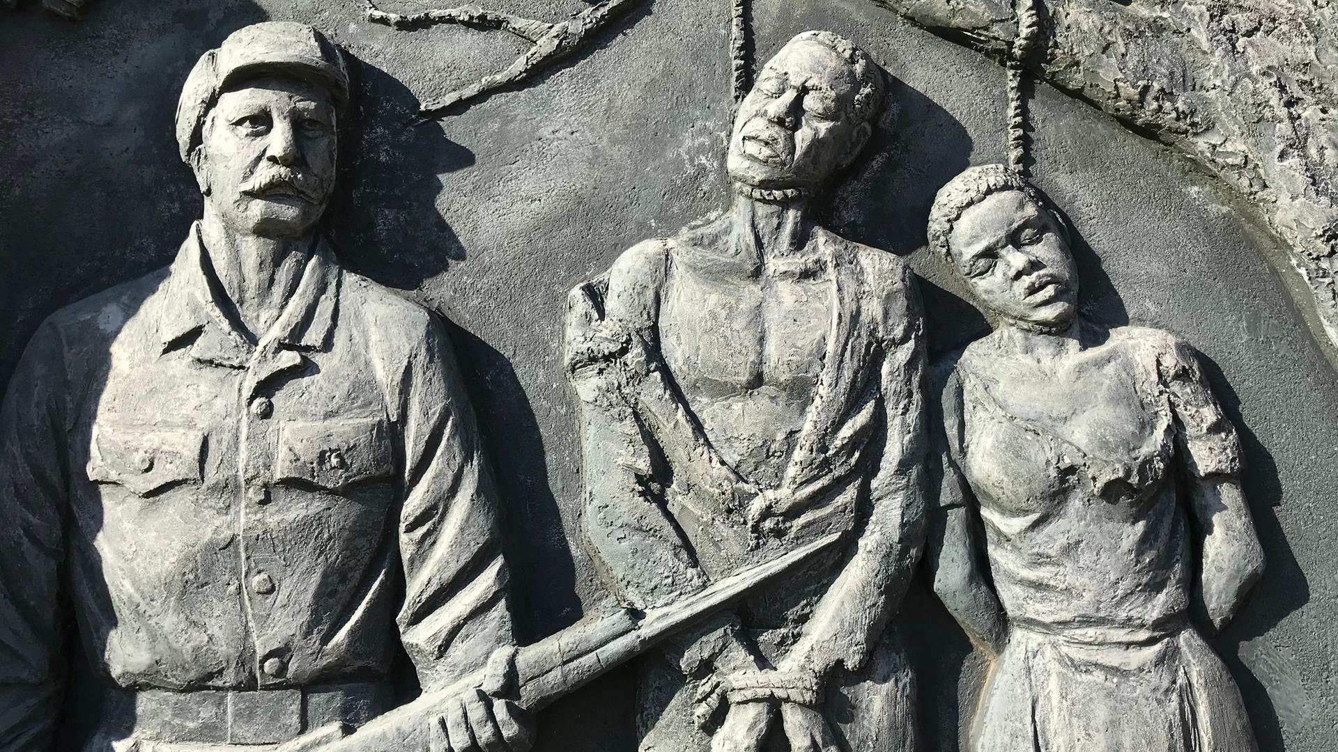 Ein Denkmal zeigt drei an einem Baum gehenkte Menschen und zwei bewaffnete Soldaten neben ihnen.