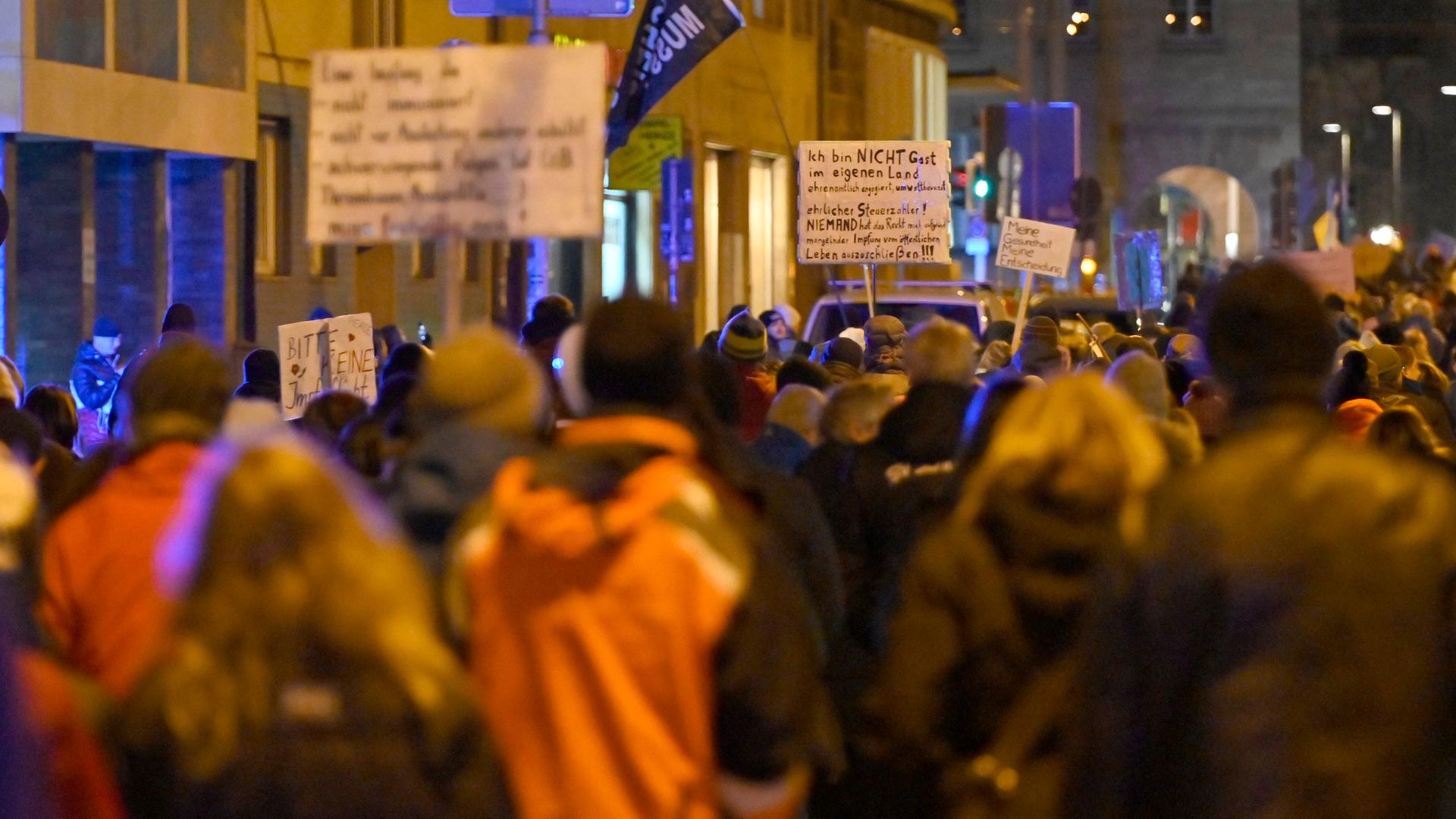 Menschen laufen am Abend mit beschriebenen Schildern durch eine Straße. Menschen laufen am Abend mit beschriebenen Schildern durch eine Straße.