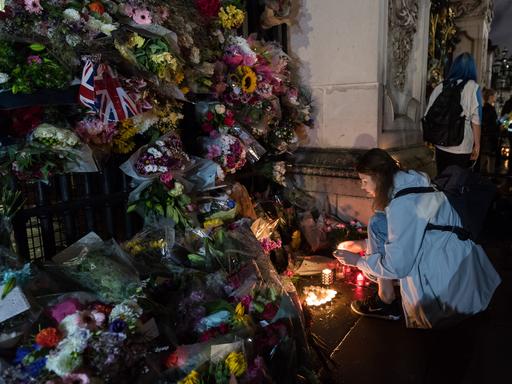 Queen Elizabeth II. ist tot: Vor dem Buckingham Palace in London zündet eine Frau eine Kerze inmitten eines Blumenmeeres an