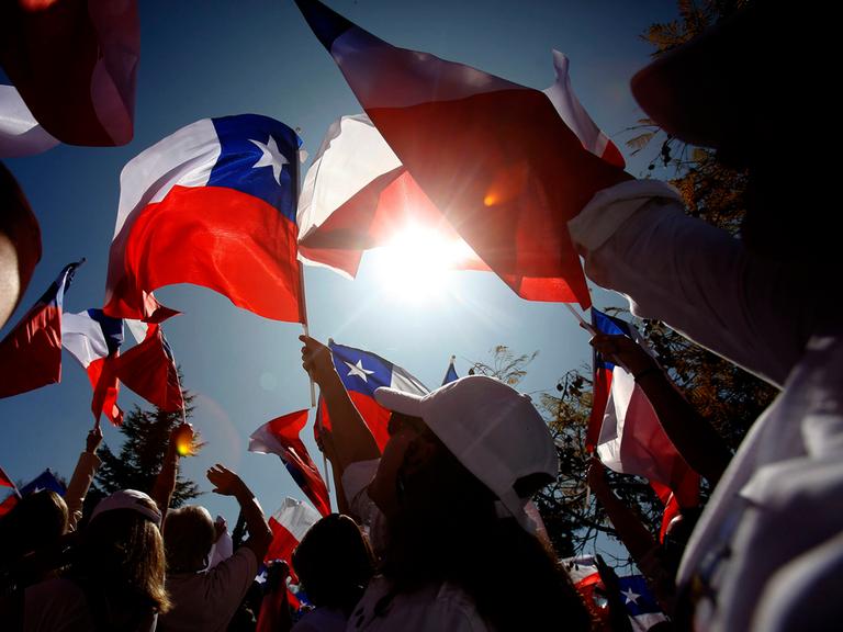 Viele Menschen treffen sich in Santiago mit ihren Flaggen, die sie der Sonne entgegen halten.