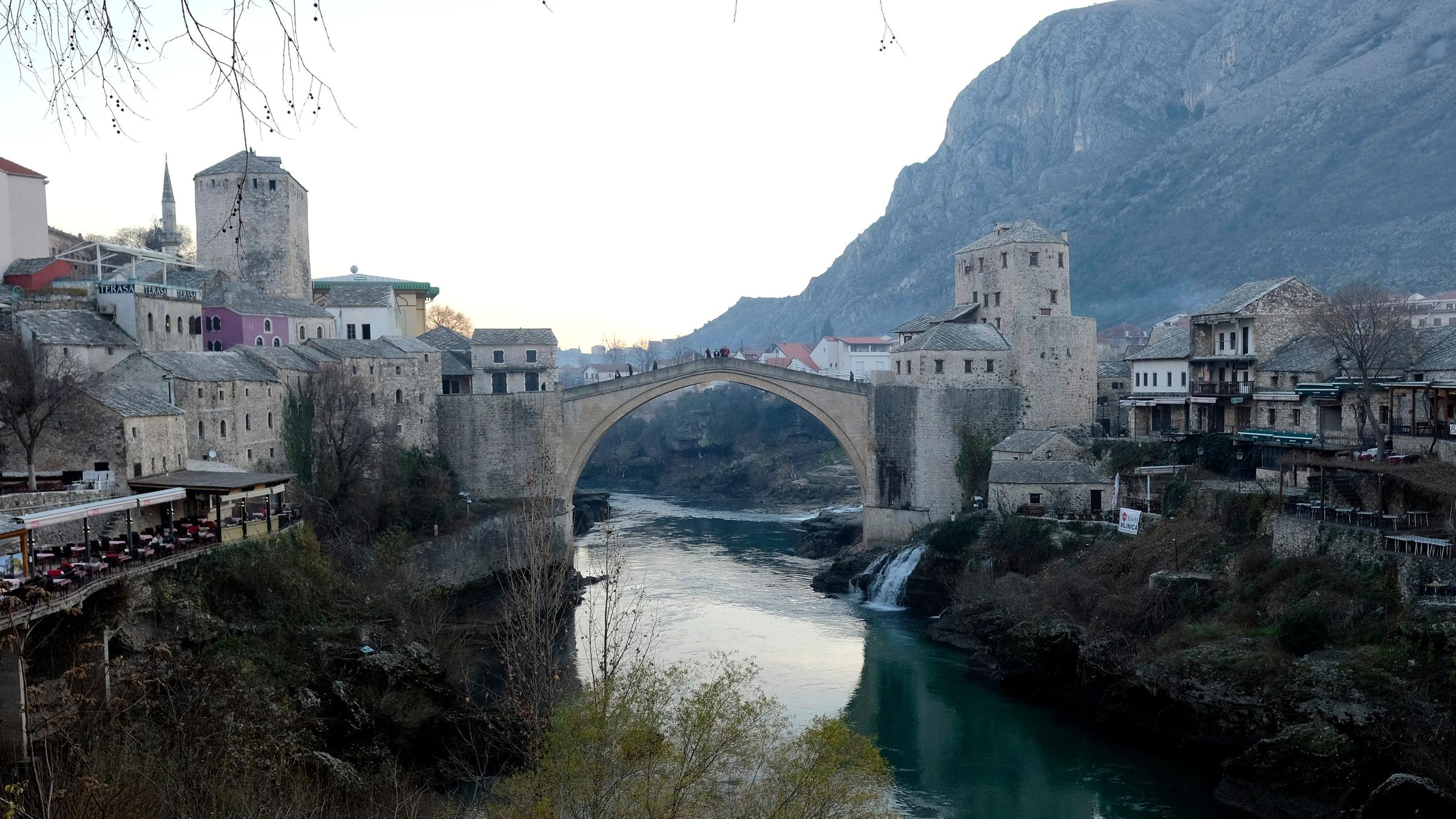 Eine Brücke führt über eine Fluss, der durch ein Tal fließt. Die Brücke verbindet Teile der Stadt Mostar.