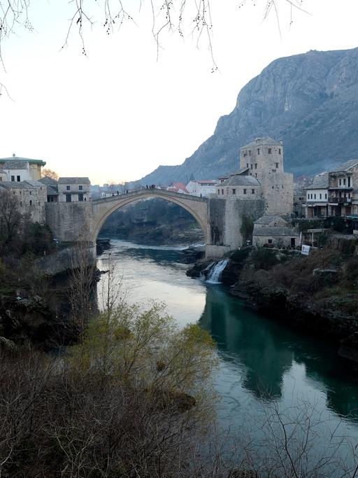 Eine Brücke führt über eine Fluss, der durch ein Tal fließt. Die Brücke verbindet Teile der Stadt Mostar.