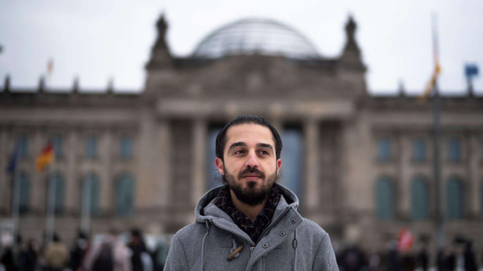 Der Grünen-Politiker Tareq Alaows steht vor dem Bundestag in Berlin und schaut seitwärts an der Kamera vorbei. Der Grünen-Politiker Tareq Alaows steht vor dem Bundestag in Berlin und schaut seitwärts an der Kamera vorbei.