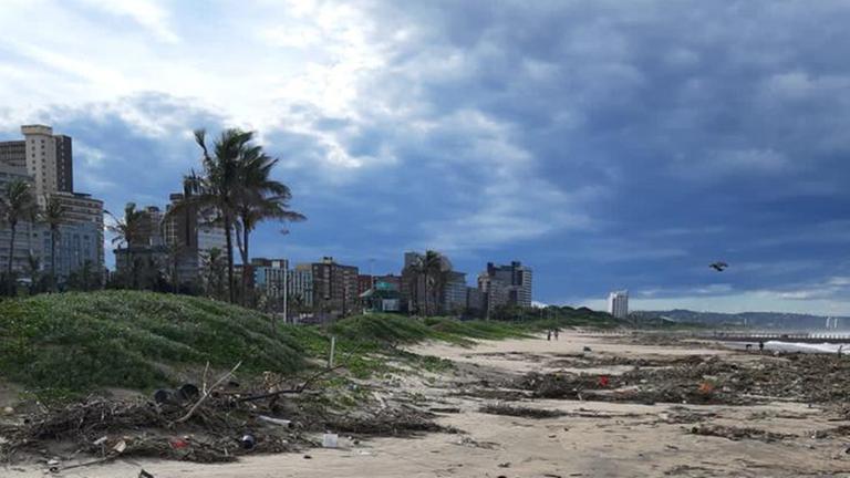 Nach Überschwemmungen in Süd-Afrika gibt es viel Müll. Dunkle Wolken ziehen übere den Strand.