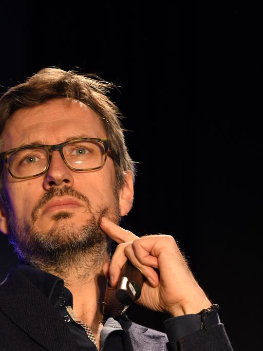 Der Produzent Jörg Winger blickt nach oben und drückt mit einem Finger der linken Hand in seine linke Wange