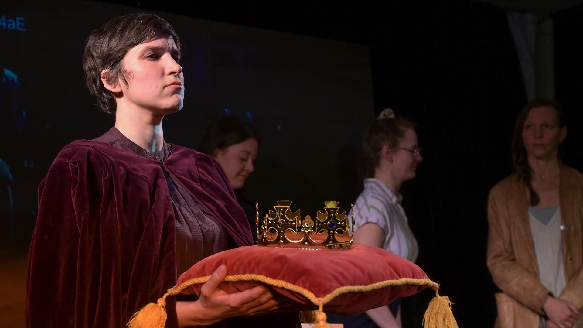 Die Schauspielerin Alessa Kordeck hält im Stück "König von Deutschland" die "Reichskrone", die auf einem Samtkissen liegt. Die Schauspielerin Alessa Kordeck hält im Stück "König von Deutschland" die "Reichskrone", die auf einem Samtkissen liegt.