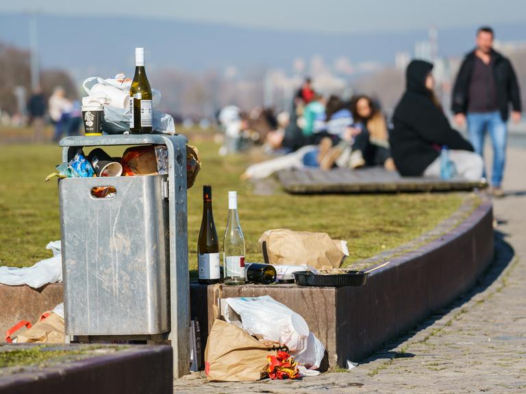 Leere Weinflaschen und weitere Hinterlassenschaften der letzten Nacht stapeln sich an einem Mülleimer am Rheinufer.