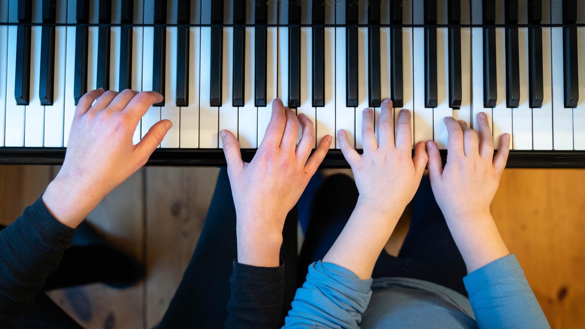 Zwei Paar Hände liegen auf einer Klaviertastatur: Eine Frau bringt einem Mädchen Klavierspielen bei. Zwei Paar Hände liegen auf einer Klaviertastatur: Eine Frau bringt einem Mädchen Klavierspielen bei.
