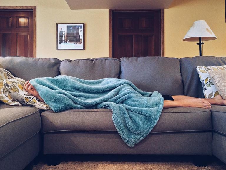 Eine Person liegt unter einer blauen Decke auf dem Sofa
