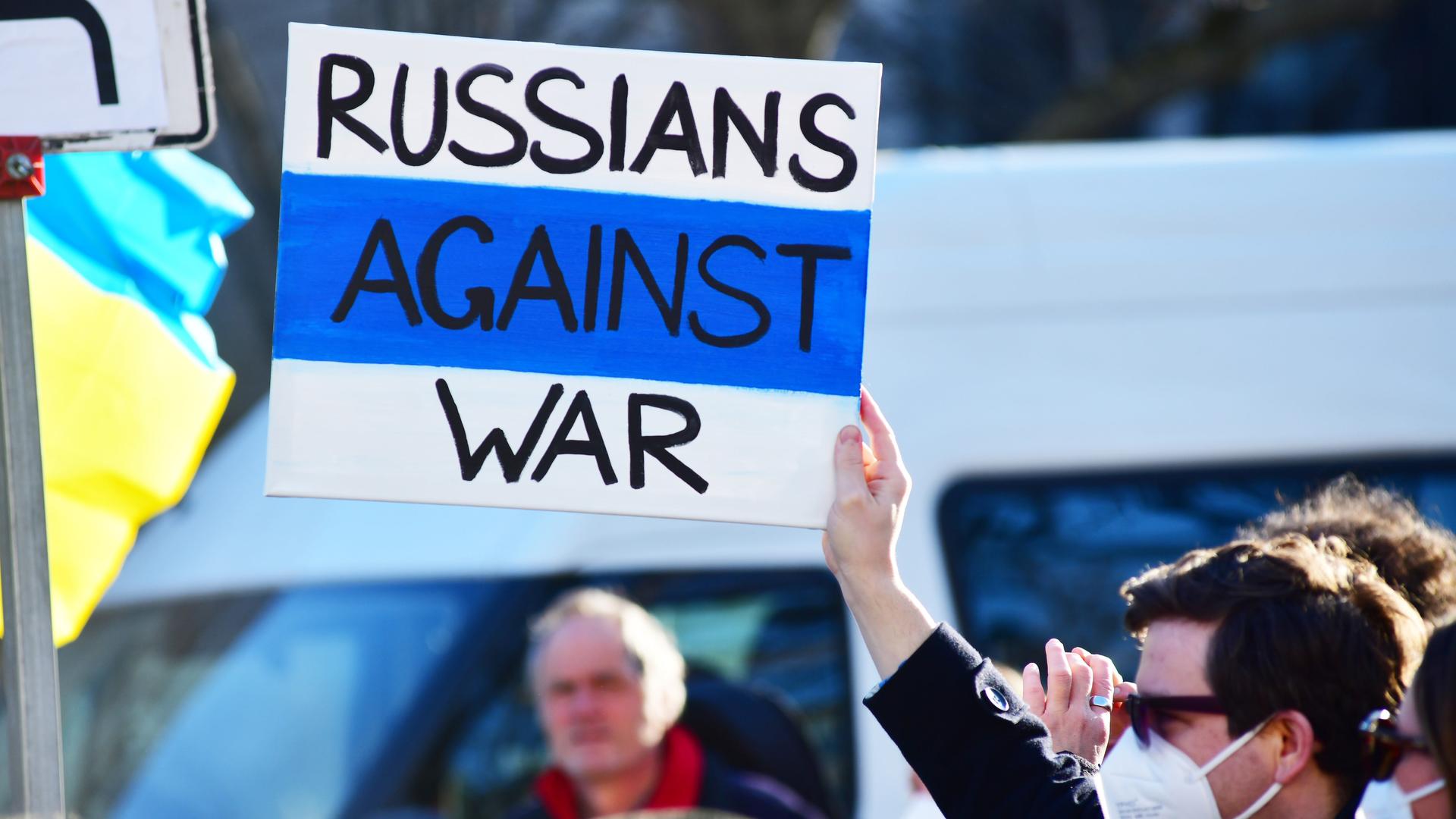 Demonstration in Berlin gegen den russischen Krieg in der Ukraine. Links sieht man eine blau-gelbe Fahne, rechts hält ein Mann ein Plakat mit der Aufschrift "Russians against War" in die Luft. Demonstration in Berlin gegen den russischen Krieg in der Ukraine. Links sieht man eine blau-gelbe Fahne, rechts hält ein Mann ein Plakat mit der Aufschrift "Russians against War" in die Luft.