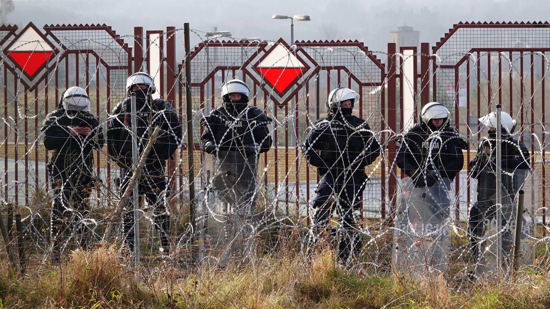 Polnische Sicherheitskräfte stehen an der Grenze hinter Stacheldraht. Polnische Sicherheitskräfte stehen an der Grenze hinter Stacheldraht.