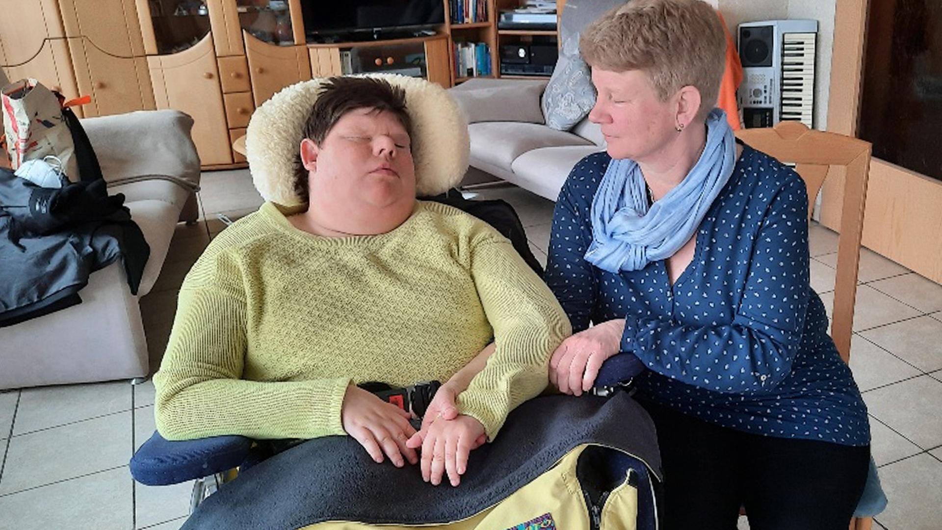 Eine Frau sitzt neben einer jungen Frau, die im Rollstuhl sitzt. Eine Frau sitzt neben einer jungen Frau, die im Rollstuhl sitzt.