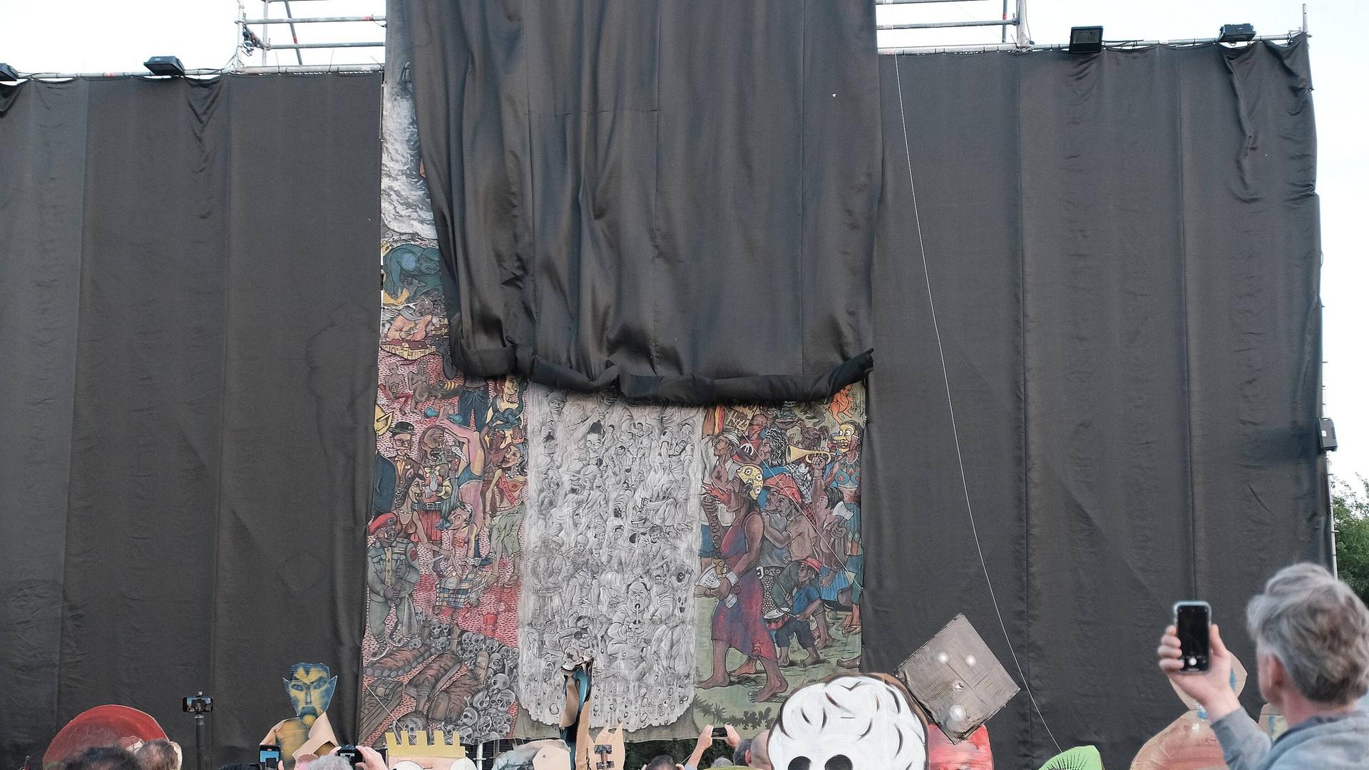 Menschen schauen zu, wie mit einem schwarzen Vorhang ein großes Kunstwerk verhüllt wird. Menschen schauen zu, wie mit einem schwarzen Vorhang ein großes Kunstwerk verhüllt wird.