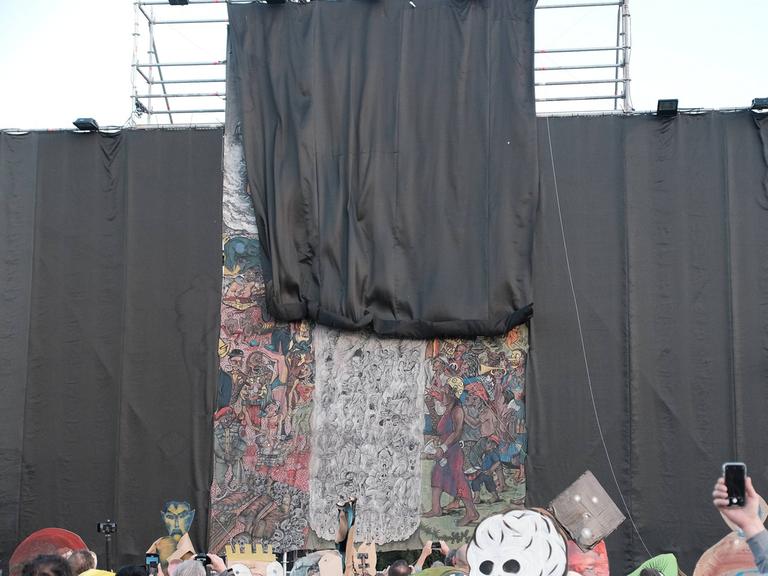 Menschen schauen zu, wie mit einem schwarzen Vorhang ein großes Kunstwerk verhüllt wird.