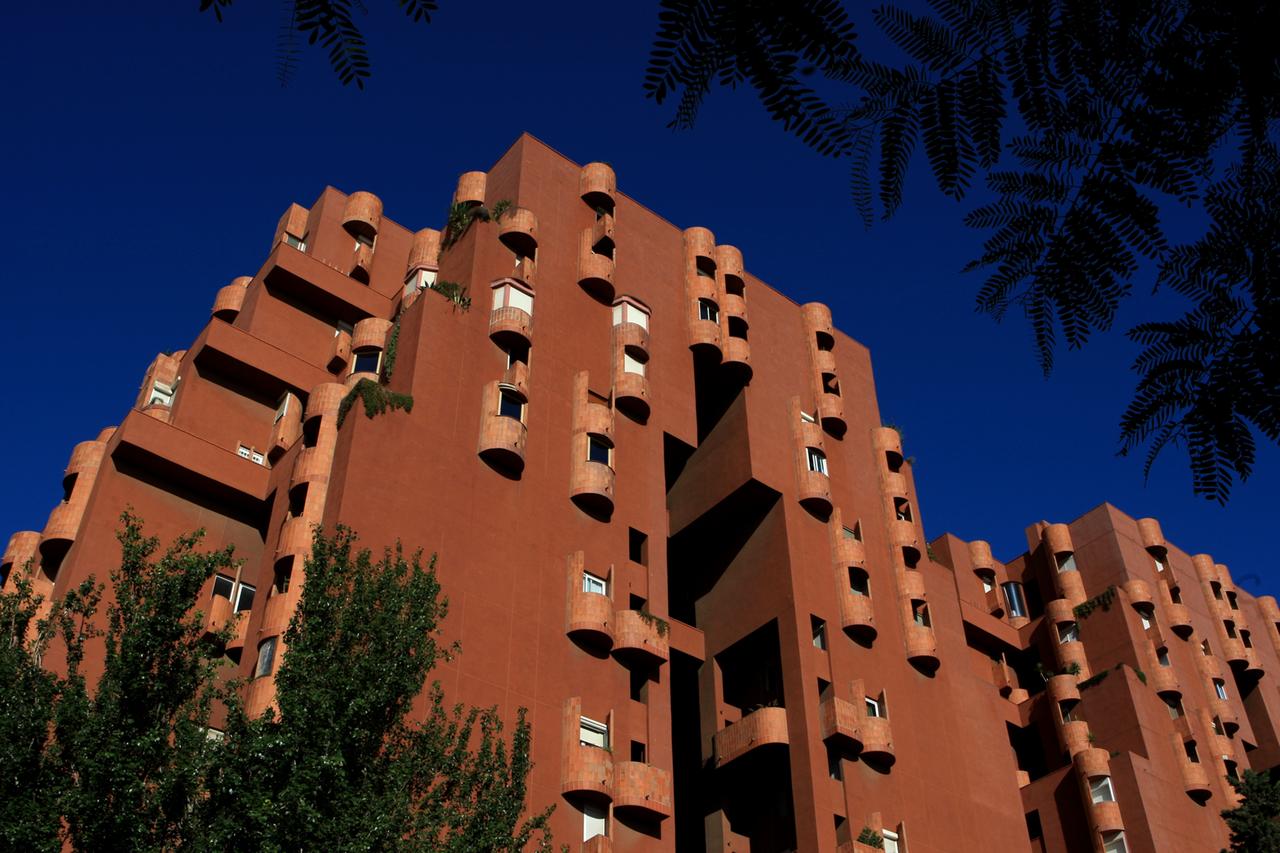 Vor dunkelblauem Himmel erhebt sich das komplett in rot gehaltene verschachtelte Gebäude 'Walden 7'. Viele der Fenster haben kleine, rundliche Balkons nach außen, was den verschachtelten Eindruck verstärkt. Vor dunkelblauem Himmel erhebt sich das komplett in rot gehaltene verschachtelte Gebäude 'Walden 7'. Viele der Fenster haben kleine, rundliche Balkons nach außen, was den verschachtelten Eindruck verstärkt.