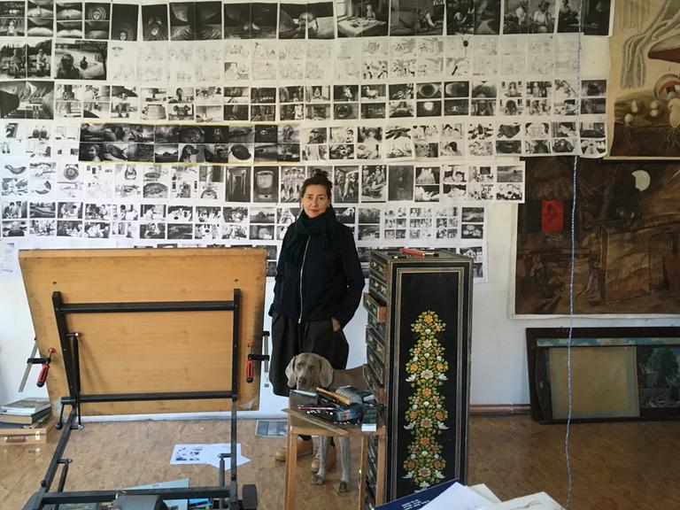 Die Zeichnerin Anke Feuchtenberger steht in ihrem Atelier vor einer Wand mit vielen Zeichnungen