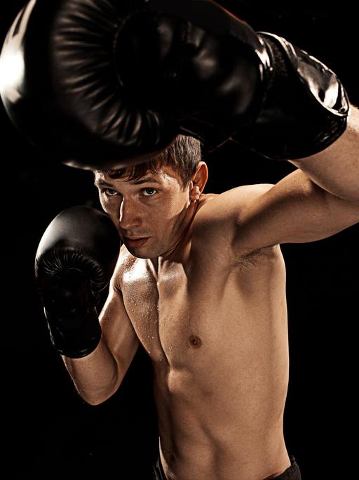 Studioaufnahme eines männlichen Boxers, der in Richtung der Kamera schlägt und versucht sich mit der anderen Hand zu schützen.