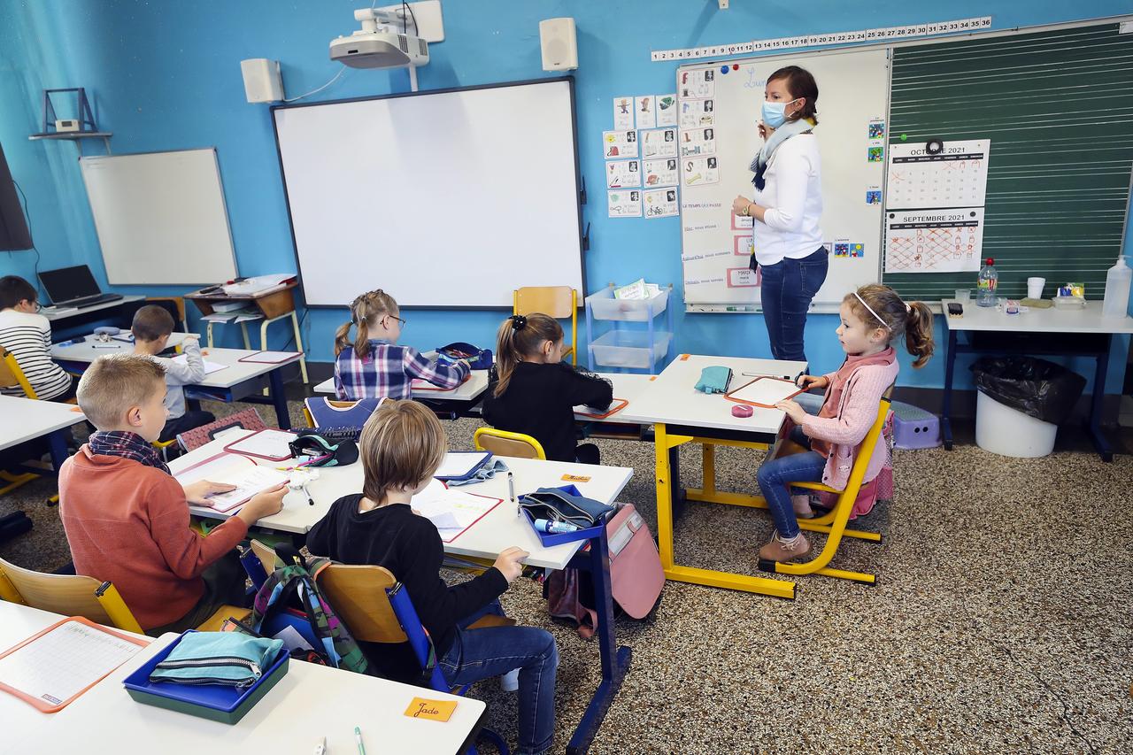 Kinder in einer Schulklasse. Sie tragen keine Masken. Vor ihnen steht eine Lehrerin, die eine Maske trägt. Kinder in einer Schulklasse. Sie tragen keine Masken. Vor ihnen steht eine Lehrerin, die eine Maske trägt.