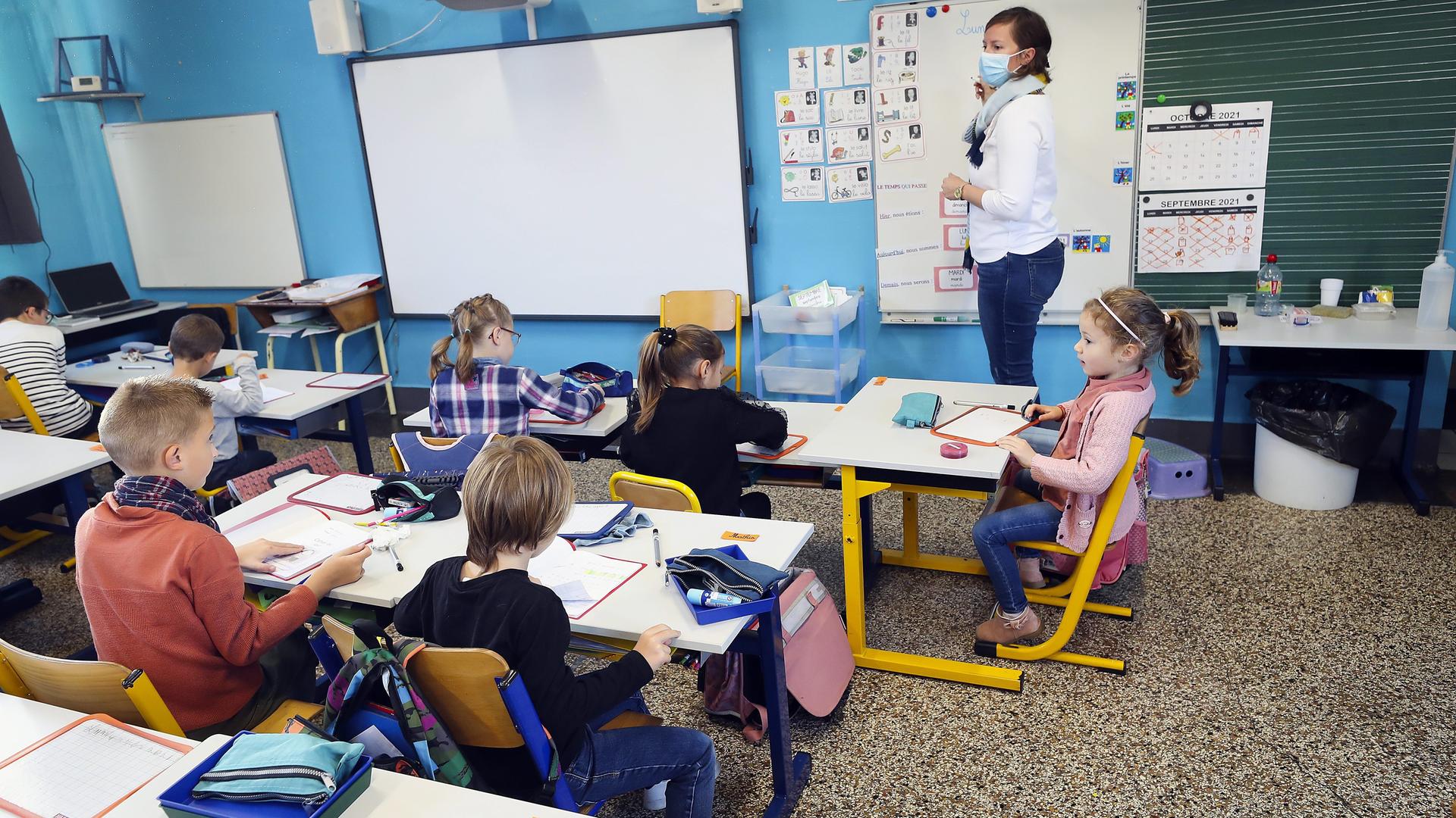 Kinder in einer Schulklasse. Sie tragen keine Masken. Vor ihnen steht eine Lehrerin, die eine Maske trägt. Kinder in einer Schulklasse. Sie tragen keine Masken. Vor ihnen steht eine Lehrerin, die eine Maske trägt.