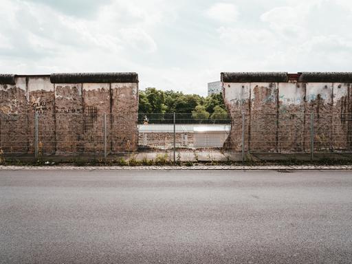 Die Berliner Mauer in der Niederkirchnerstraße 1 im Jahr 2019. In der Mitte ist ein großes Loch, durch das man hindurchsehen kann.