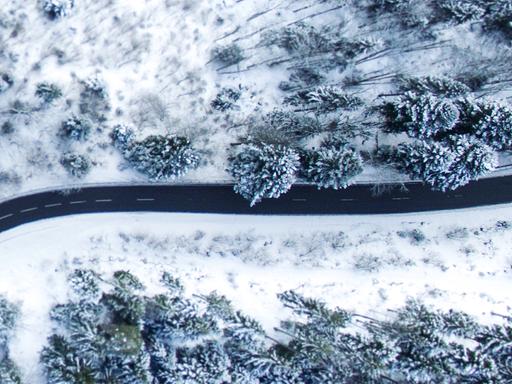 Eine sich schlängelnde Straße in verschneiter Waldlandschaft aus der Vogelperspektive.