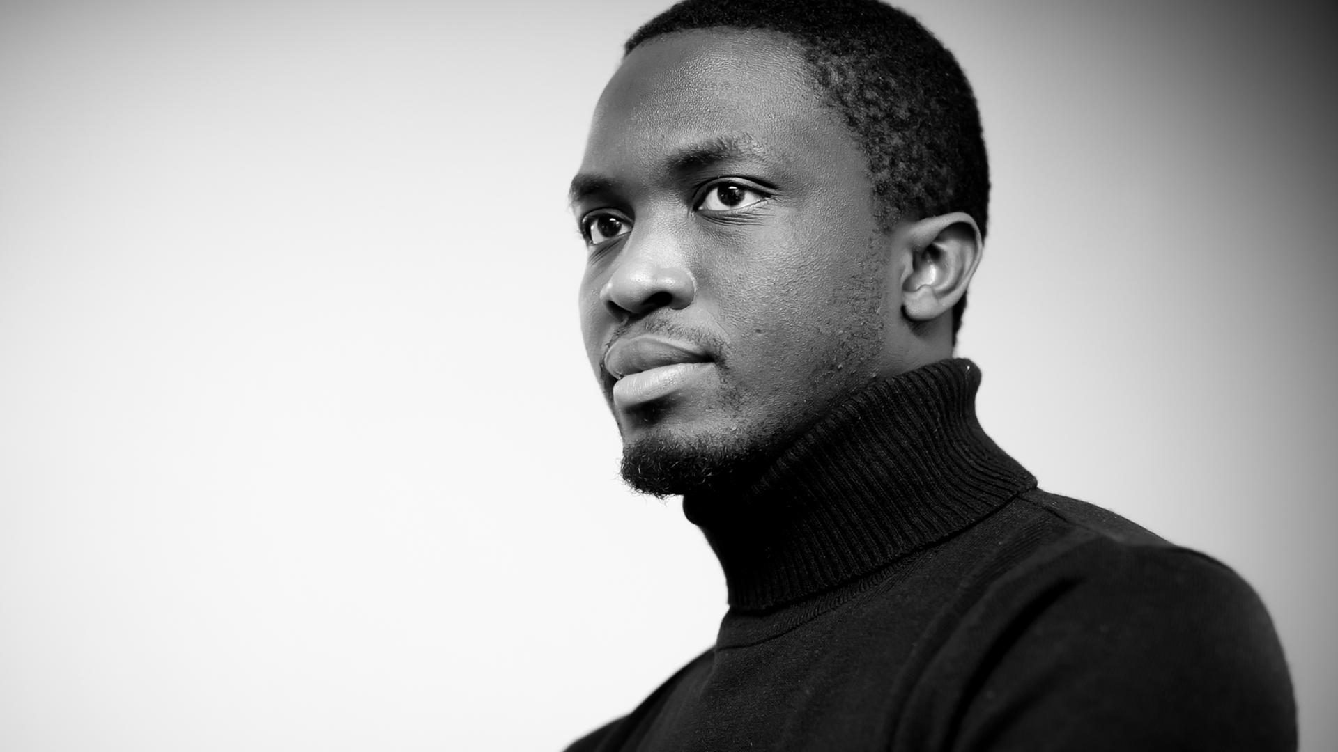 Der senegalesische Autor Mohamed Mbougar Sarr. Es handelt sich um ein Schwarzweiß-Foto, der Autor trägt einen dunklen Rollkragenpullover. Der senegalesische Autor Mohamed Mbougar Sarr. Es handelt sich um ein Schwarzweiß-Foto, der Autor trägt einen dunklen Rollkragenpullover.