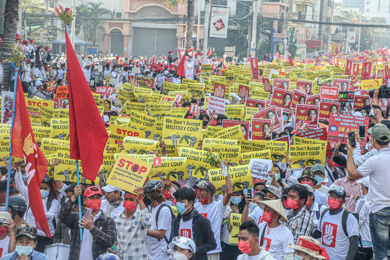 Tausende Menschen laufen in der Stadt Mandalay mit Protesplakaten eine Straße entlang. Tausende Menschen laufen in der Stadt Mandalay mit Protesplakaten eine Straße entlang.