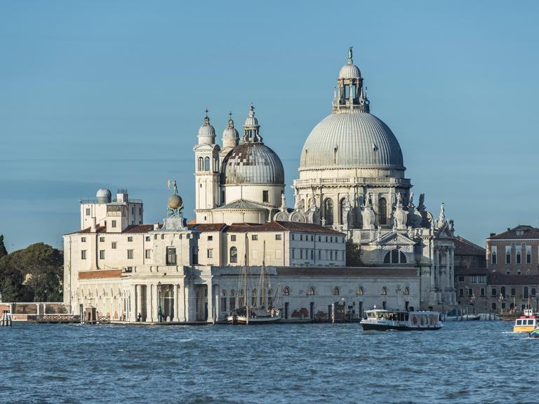 Wir sehen eine barocke Kirche, die an der Einfahrt zum Canal Grande in Venedig steht. 