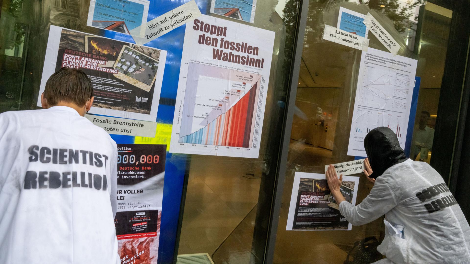 Aktivisten der Klimabewegung "Scientist Rebellion" kleben Plakate mit Fakten über die Erderwärumg an eine Filiale der Deutschen Bank in München. Aktivisten der Klimabewegung "Scientist Rebellion" kleben Plakate mit Fakten über die Erderwärumg an eine Filiale der Deutschen Bank in München.