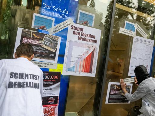 Aktivisten der Klimabewegung "Scientist Rebellion" kleben Plakate mit Fakten über die Erderwärumg an eine Filiale der Deutschen Bank in München. 